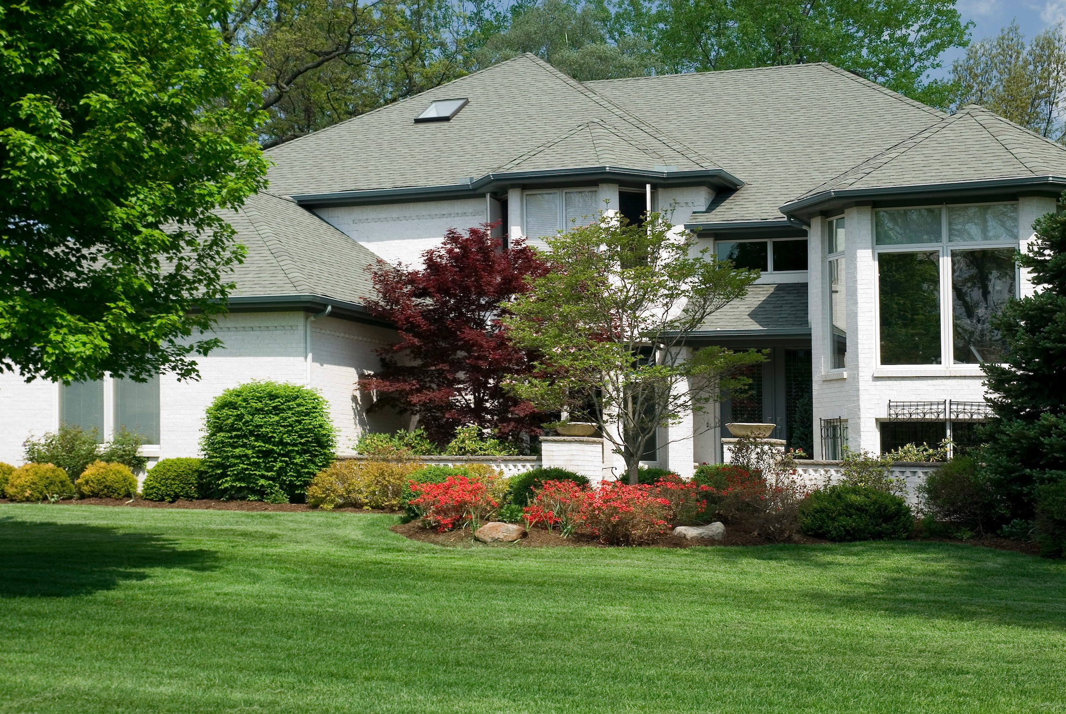 Beautiful two story white brick home featuring some nice architectural details and colorful landscaping.
